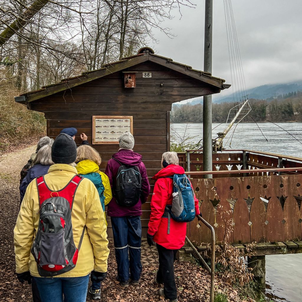Die Wandergruppe schaut auf ein Bild, das an einem Fischerhäuschen hängt.