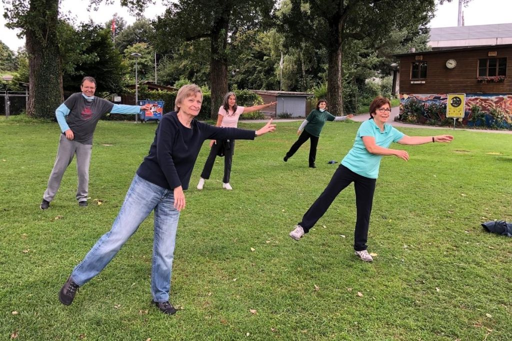 Fünf Personen unterschiedlichen Alters treiben in einem Park gemeinsam Sport.