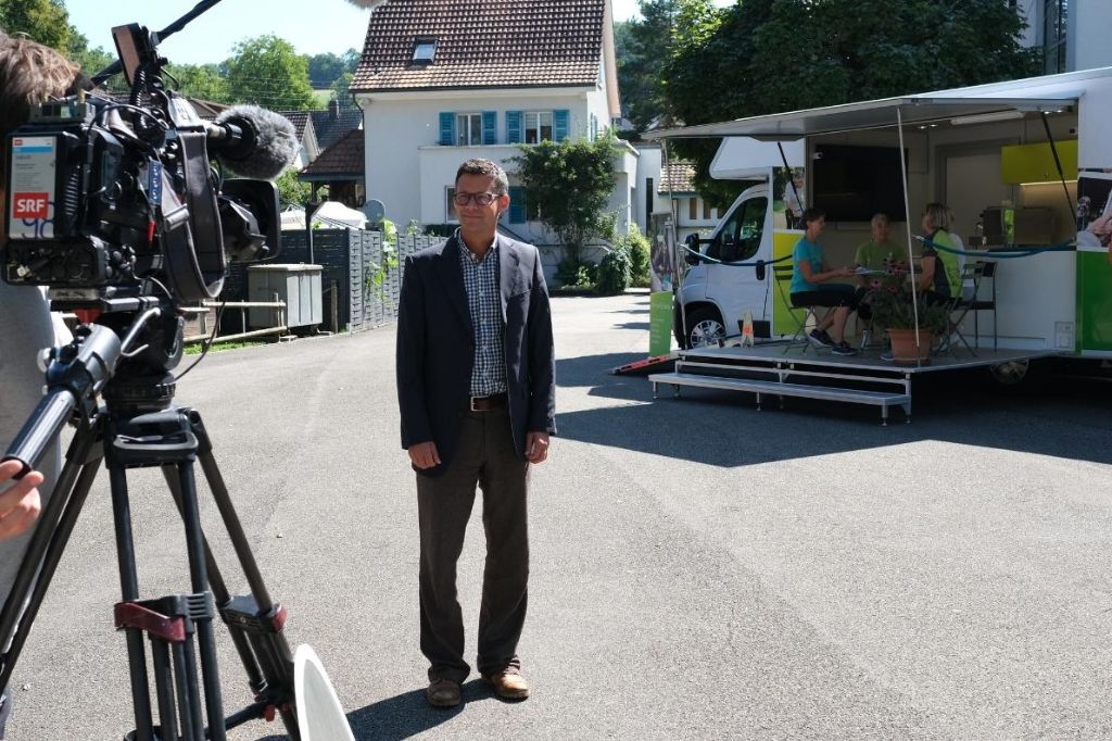 Geschäftsleiter wird vor dem Infobus von SRF gefilmt.