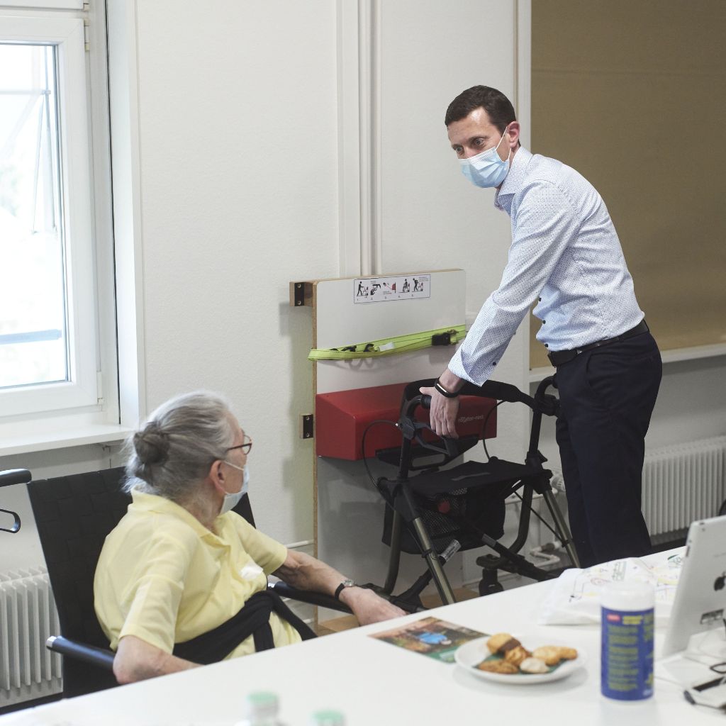 Kundin sitzt in einem Rollstuhl am Tisch eines Sitzungszimmers und unterhält sich mit Mitarbeiter.