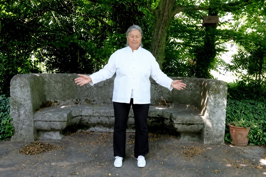 Seniorin befindet sich im Freien und praktiziert die Meditationsform Qigong.
