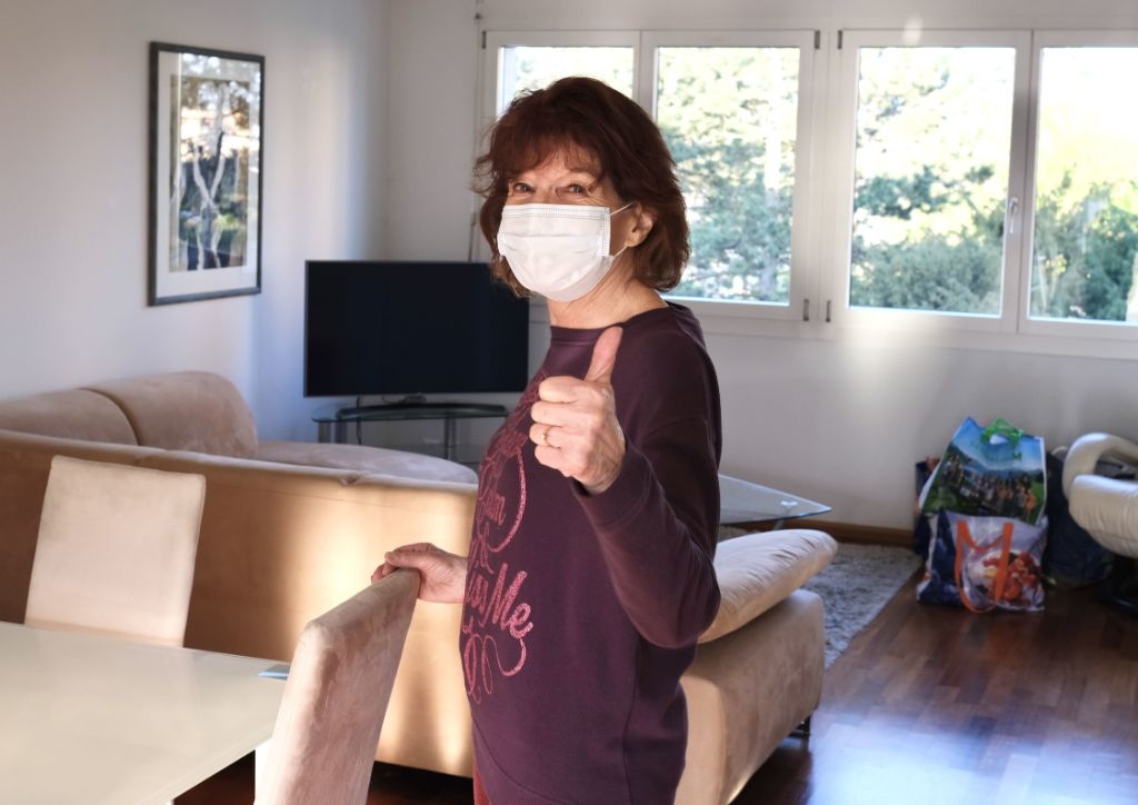 Seniorin befindet sich in ihrem Wohnzimmer und hebt nach einem Umzug die Daumen in die Höhe.