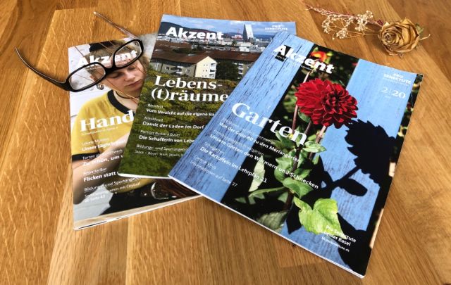 Drei Exemplare des Akzent Magazins liegen auf einem Holztisch.