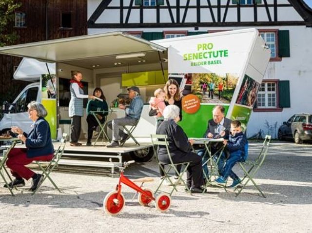 Vor Infobus unterhalten sich Personen unterschiedlichen Alters und nehmen an Aktivitäten teil.