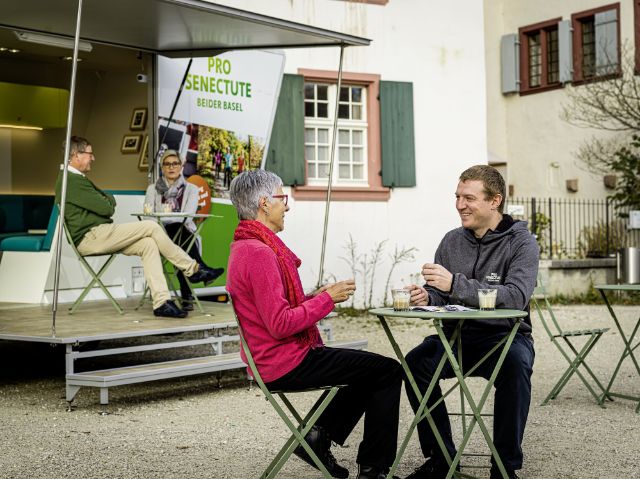 Ein Mitarbeiter informiert eine Kundin über unsere Angebote, eine Mitarbeiterin sitzt mit einem Kunden im Infobus.