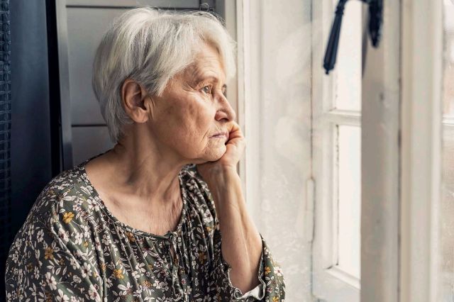 Eine einsame Seniorin schaut traurig aus ihrem Fenster.