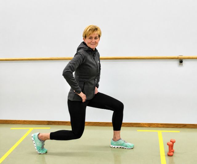 Sportliche Kursleiterin zeigt in einer Turnhalle verschiedene Übungen vor.
