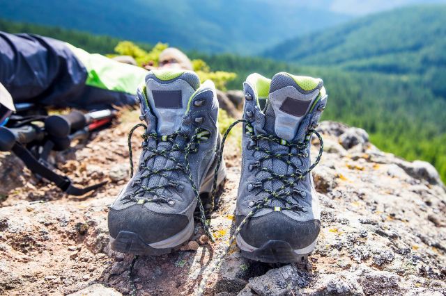Wanderschuhe auf steinigem Untergrund und Waldlandschaft im Hintergrund.