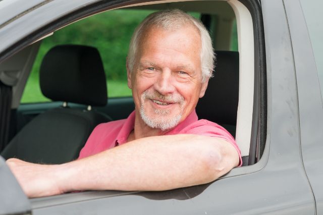 Ein älterer Kurierdienstmitarbeitender sitzt im Auto und lächelt.