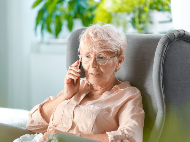 Seniorin sitzt in einem Sessel und führt ein beratendes Telefongespräch.