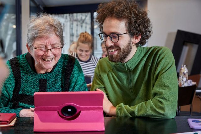 Ein junger Mann zeigt einer Seniorin die verschiedenen Funktionen auf ihrem Tablet.