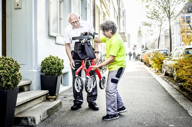 Berater zeigt einem Kunden draussen wie der Rollator zusammengeklappt werden kann.