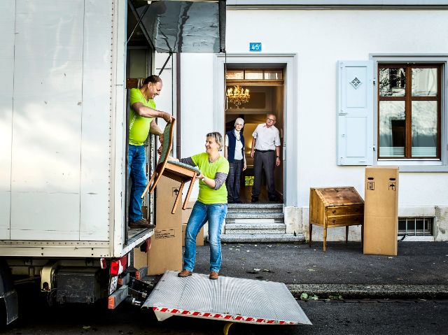 Zwei Mitarbeitende helfen einem älteren Ehepaar bei ihrem Umzug.