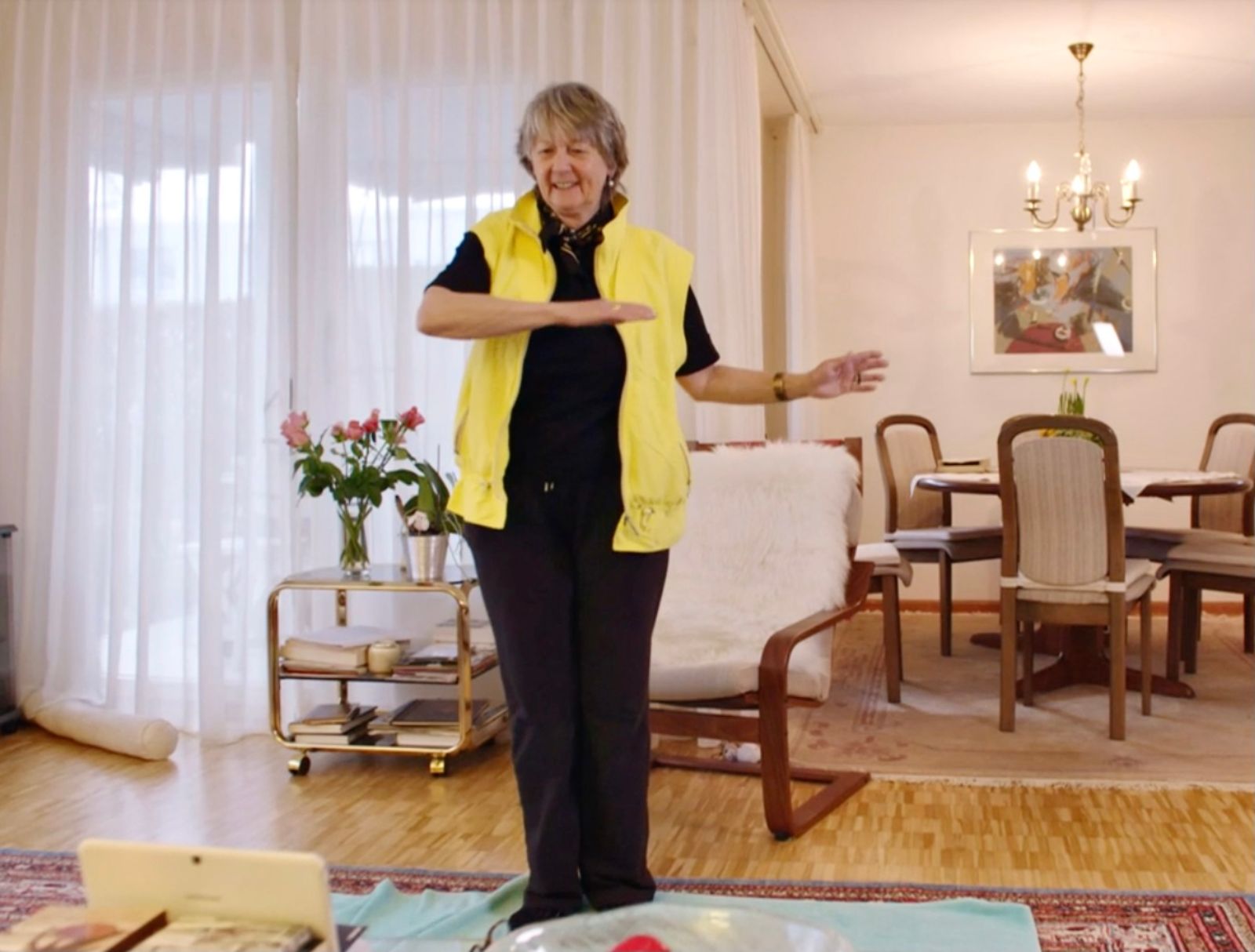 Seniorin nimmt im Wohnzimmer dank ihres iPads online an einem Fitnessangebot teil.