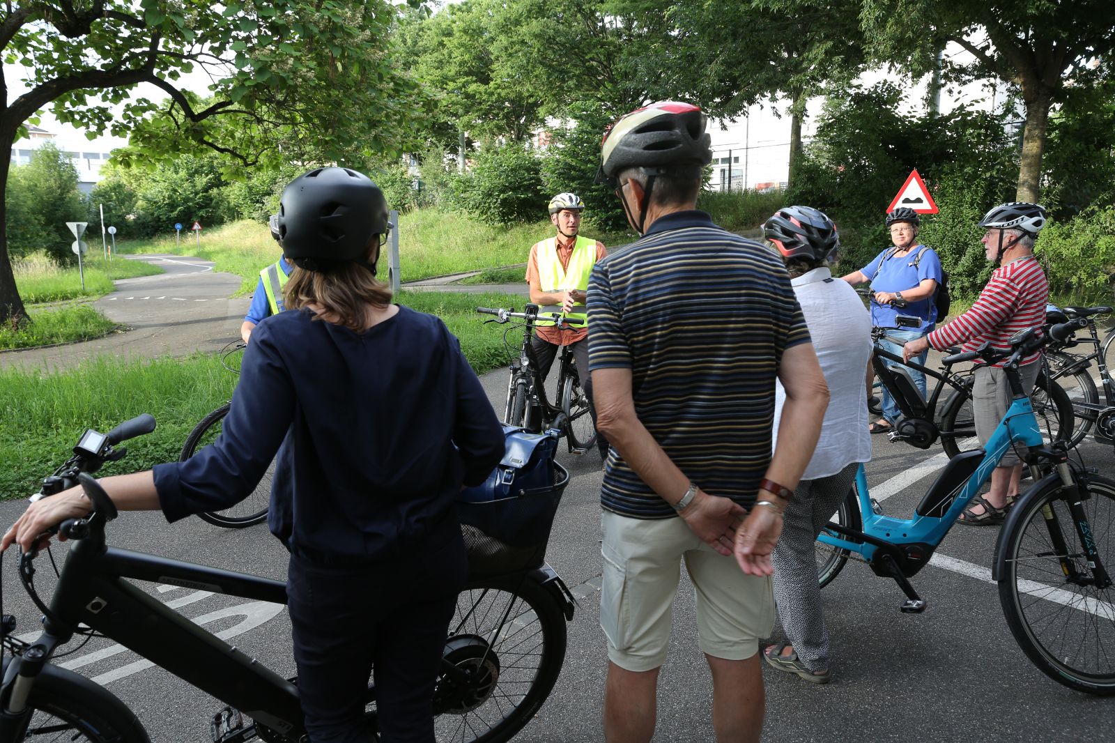 Personen unterschiedlichen Alters hören den Leitern des E-Bike-Kurses auf einem Ausflug zu.